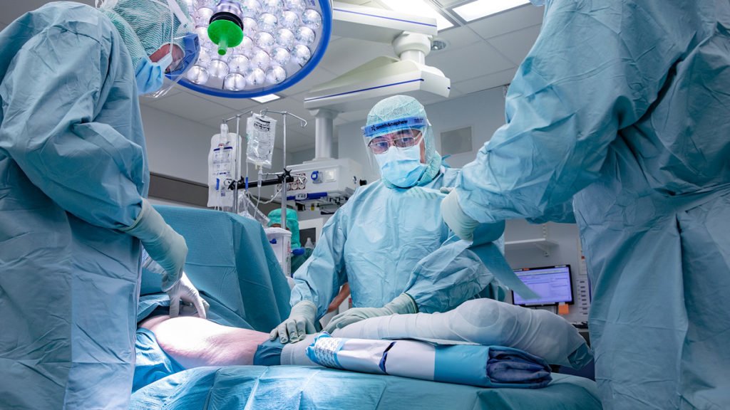 Bild på vårdpersonal, iklädda sterila skyddskläder och ansiktsmasker i en operationssal.