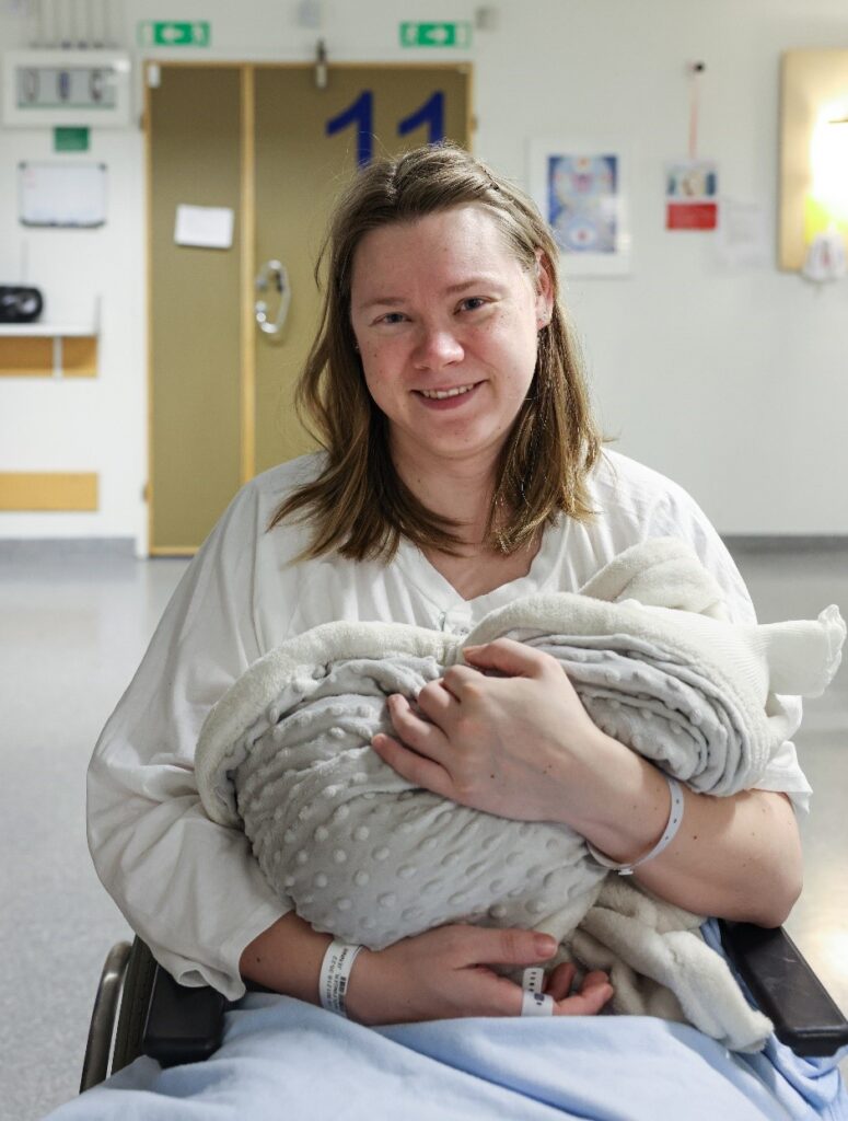 En kvinna sitter i en rullstol och har ett nyfött barn i sin famn.