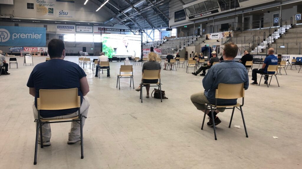 Personer som sitter och väntar efter att ha blivit vaccinerade i en idrottsarena