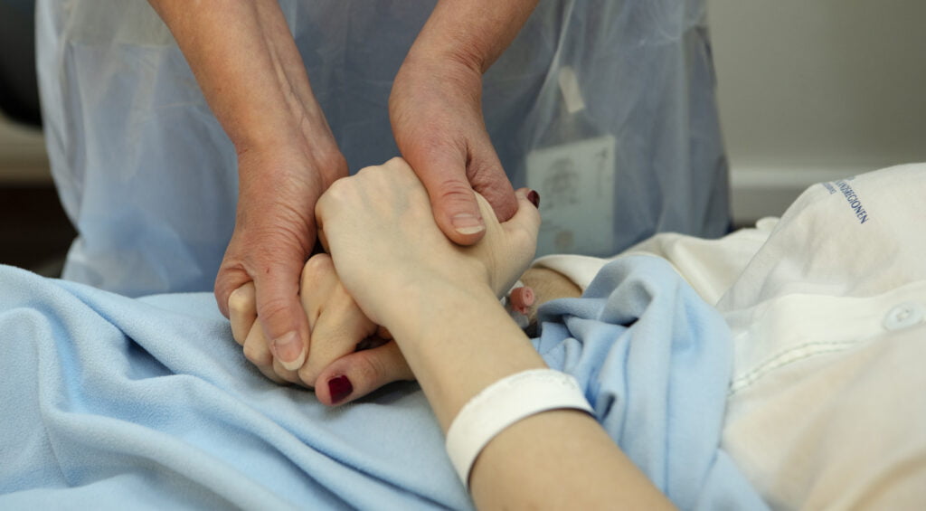 vårdpersonal kramar om en patients hand.