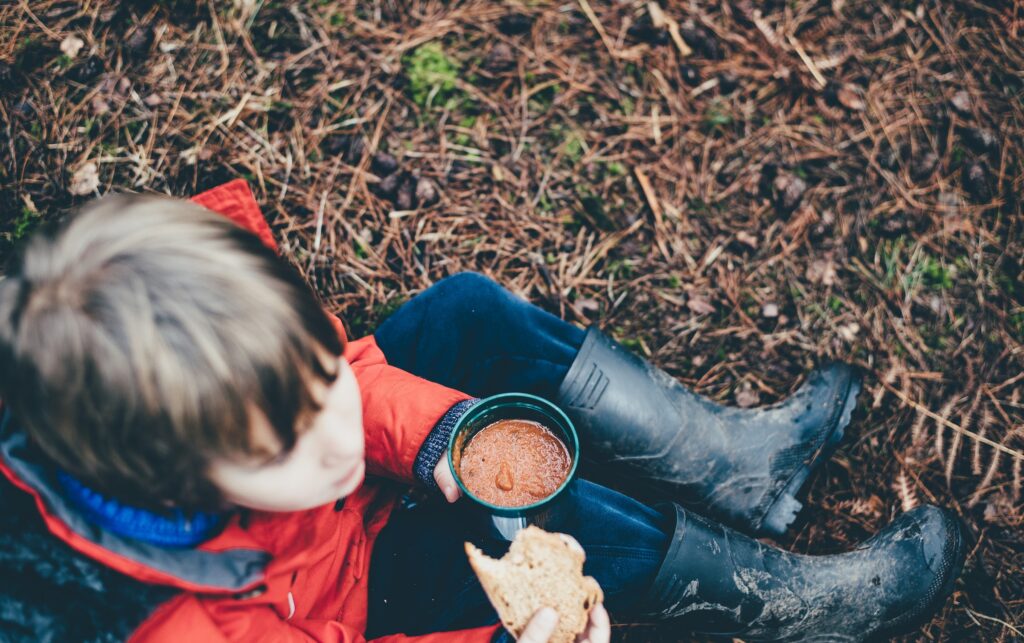 pojke sitter på marken med en kopp soppa i handen