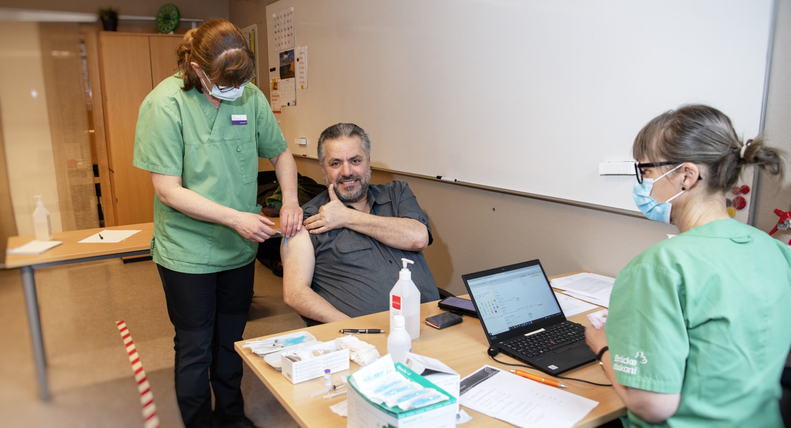 . Jamal Alhammod gör tummen upp när Zari Falknäs Abelsson vaccinerar honom. Carina Persson för in uppgifterna i datorn.