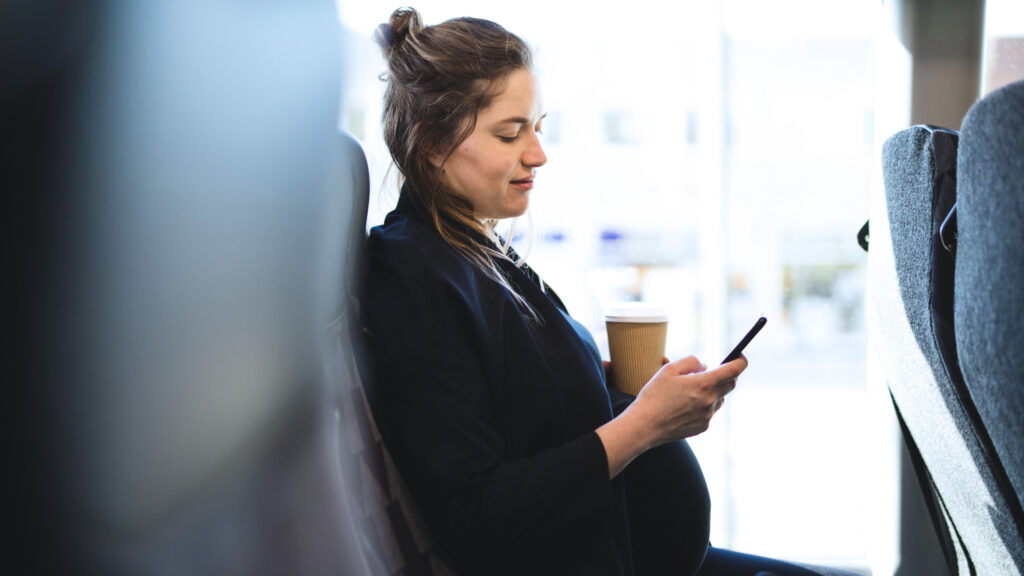Gravid kvinna sitter och tittar på en mobiltelefon.