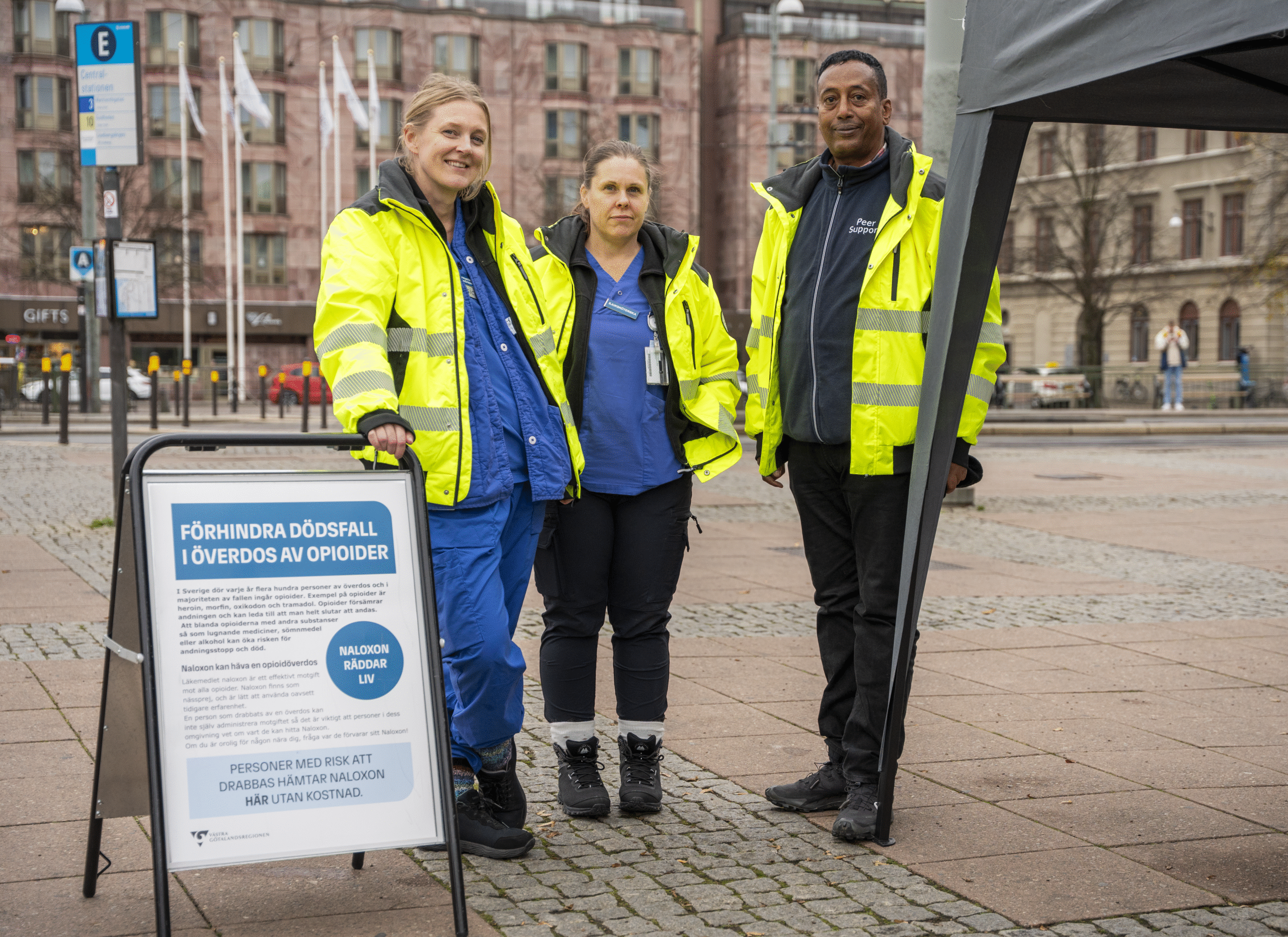 Tre personer står på ett torg utomhus.