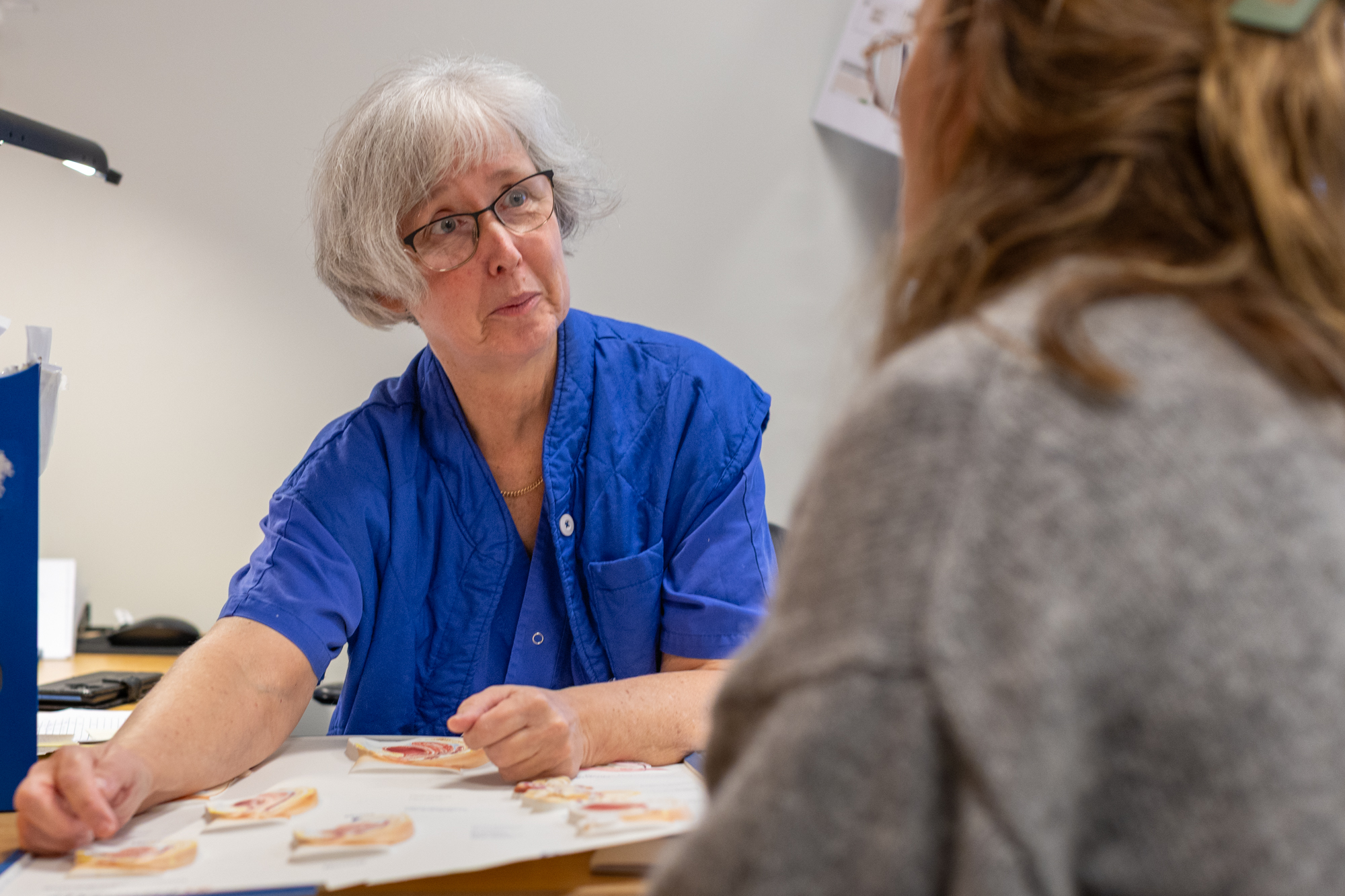 Kvinna i vårdkläder sitter vid ett bord.