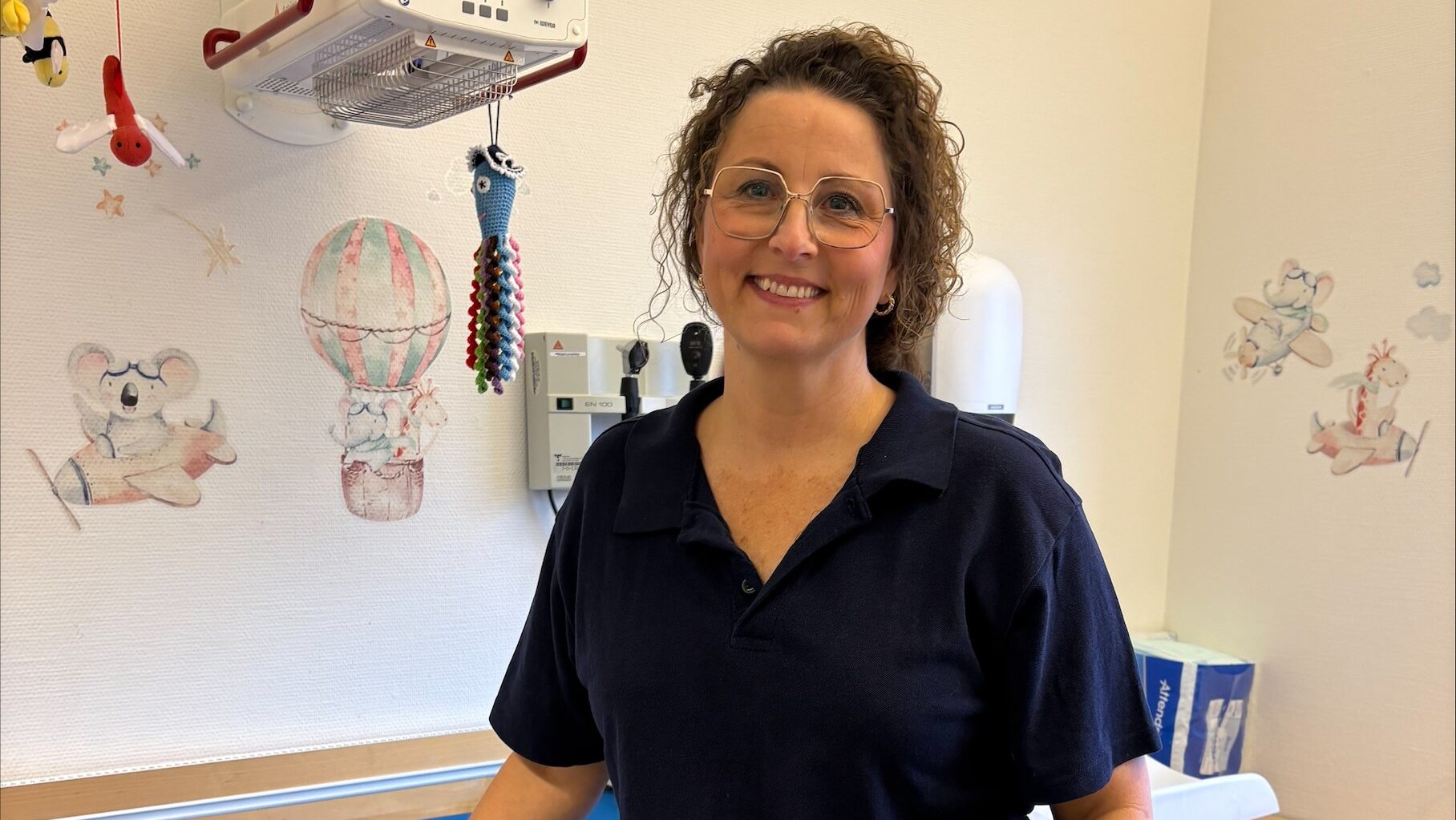 En kvinna i vårdklädsel står vid ett undersökningsbord för små barn.