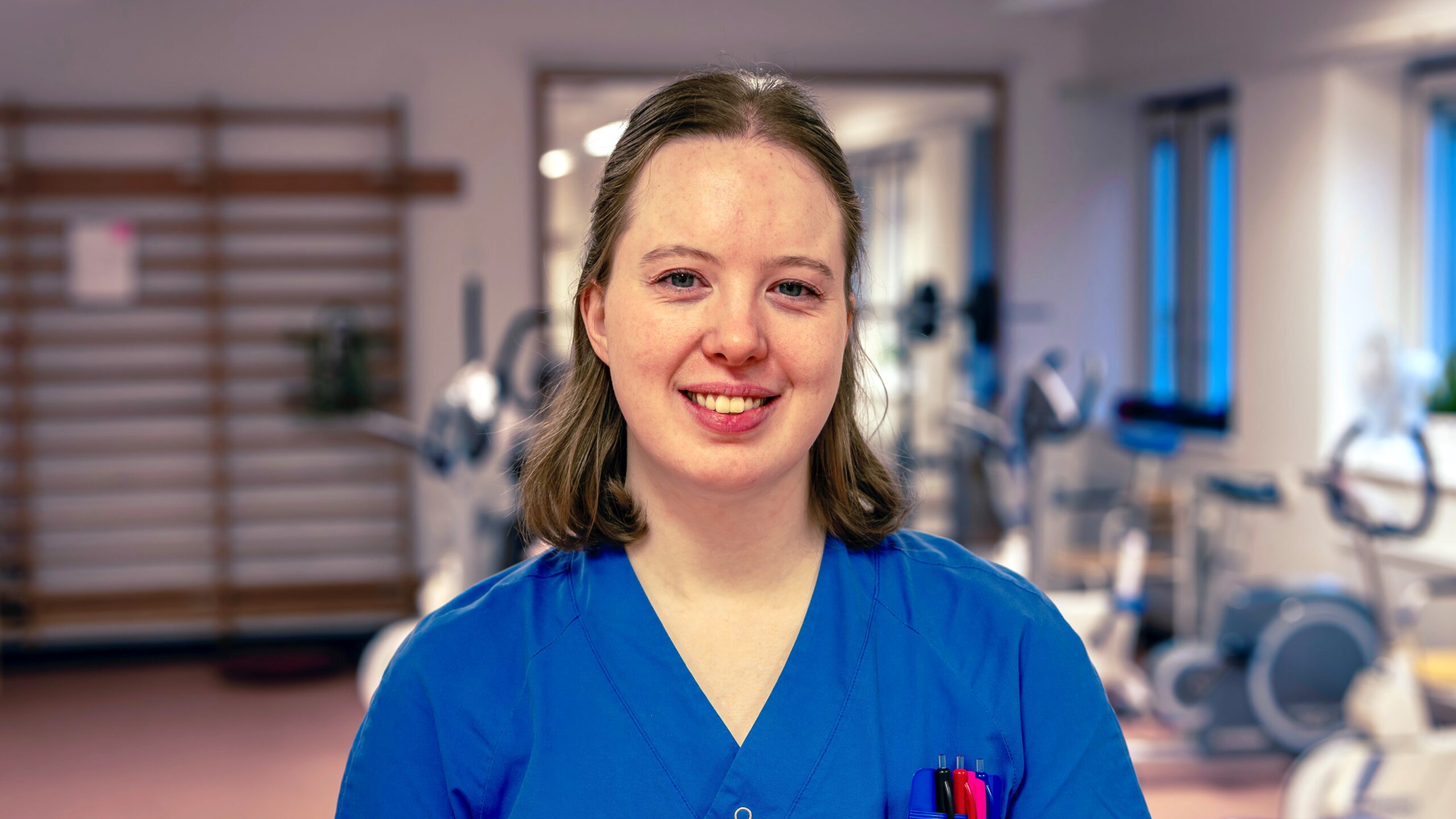 Kvinna i vårdkläder står upp inomhus.