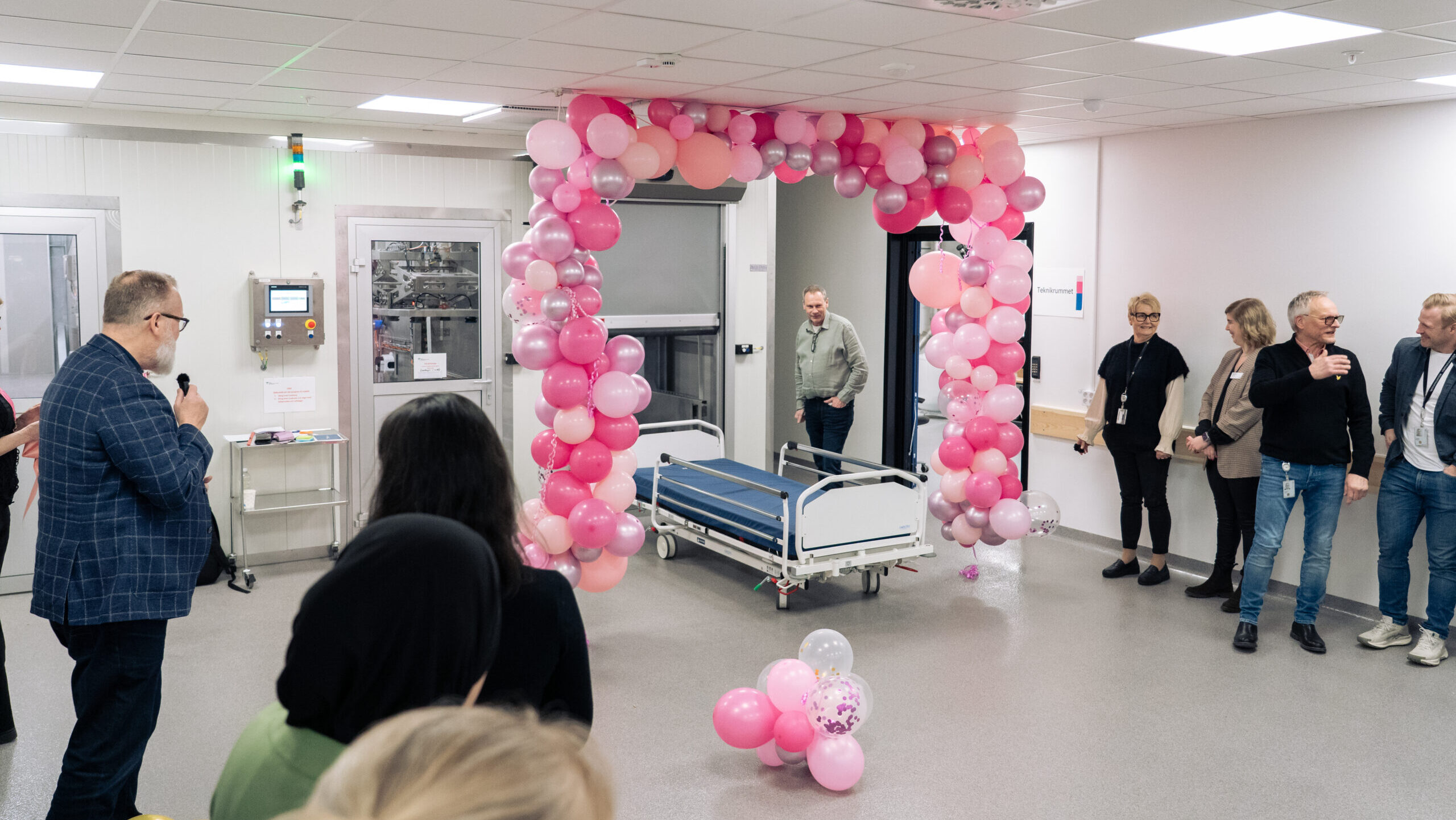 En sjukhussäng, rosa ballonger och flera personer.