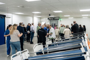 Flera sjukhussängar i ett rum där det också står personer.