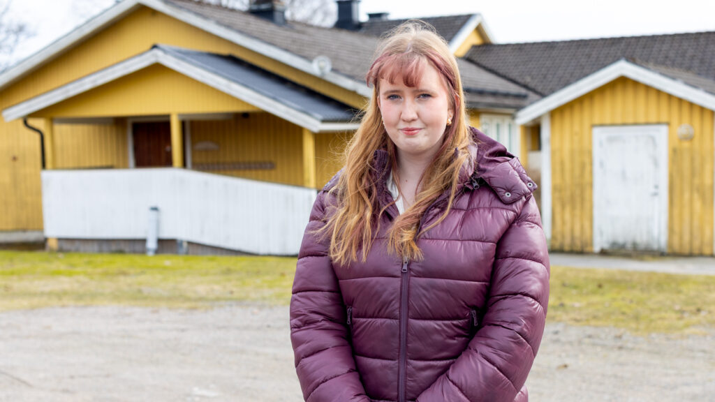 En kvinna står utomhus framför ett gult hus.