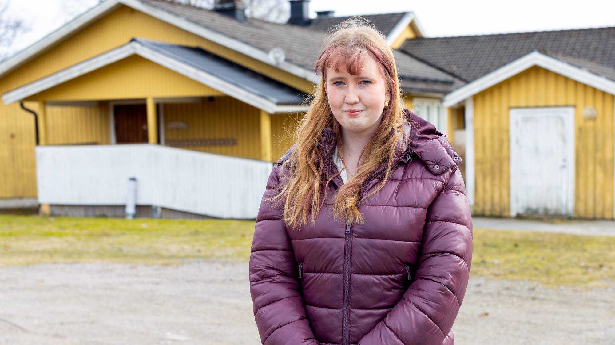 En kvinna står utomhus framför ett gult hus.