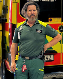 En man i vårdkläder står framför en ambulans.