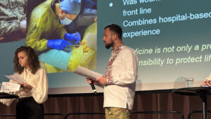 Person på scen med bild på en operation i bakgrunden.