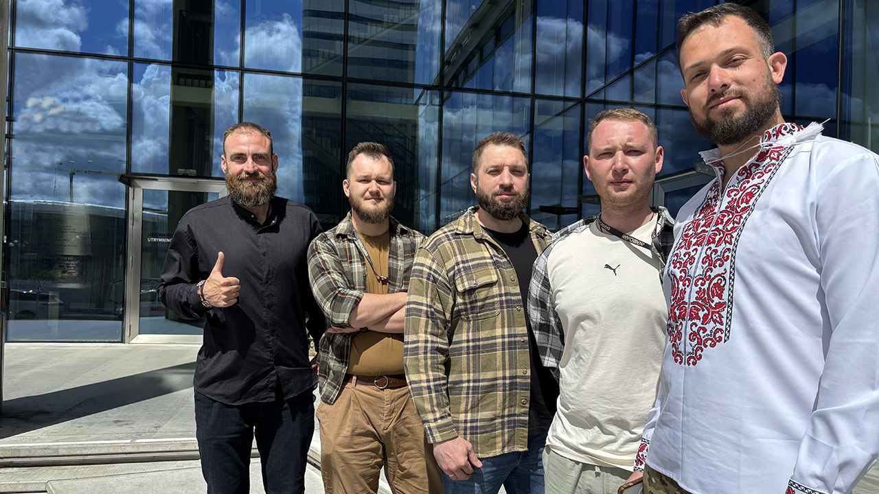Fem personer framför ett stort glasfönster.