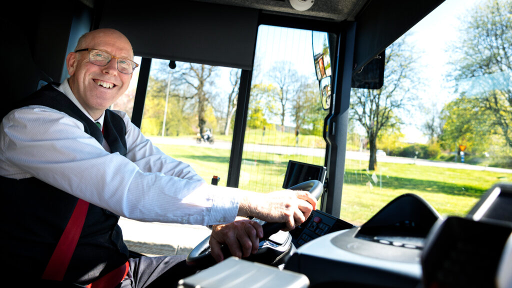 En busschaufför som sitter på förarplatsen i en buss.