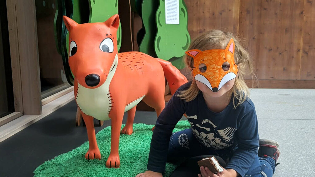 En räv och ett barn med mask framför ansiktet.