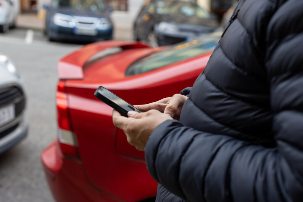 En person håller en mobiltelefon i handen. Personen är utomhus.