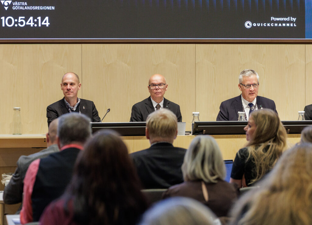 Tre män vid ett podium på ett politiskt möte.